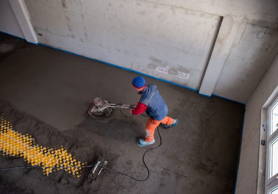 Laborer performing and polishing sand and cement screed floor on the construction site of a new two-level apartment. Sand and cement floor screed